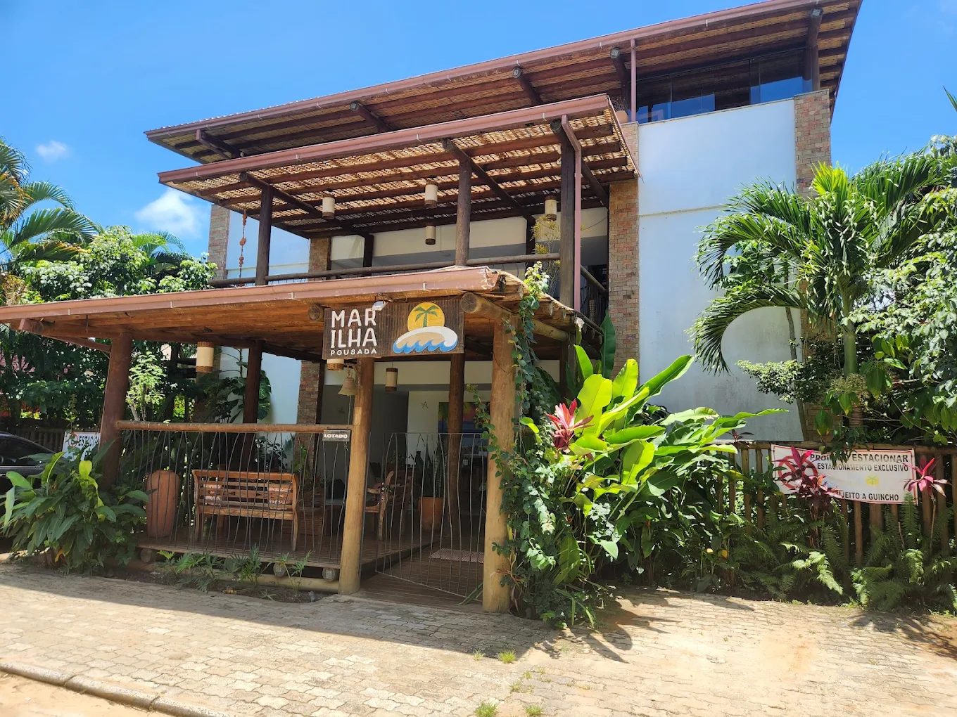 Fachada da Mar Ilha Pousada, com varandas de madeira e jardim tropical, em dia de sol